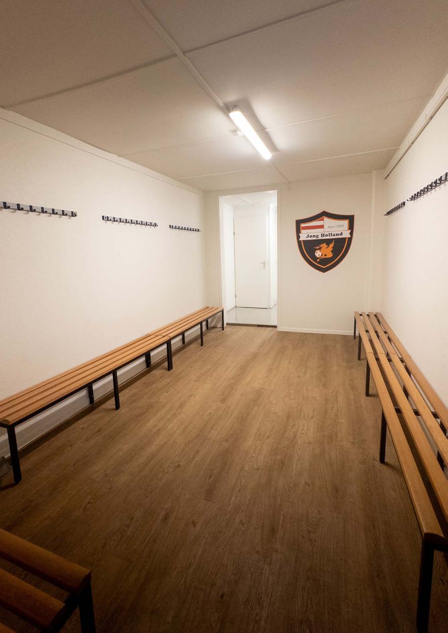 De gerenoveerde kleedkamer met houten banken en het clublogo op de muur