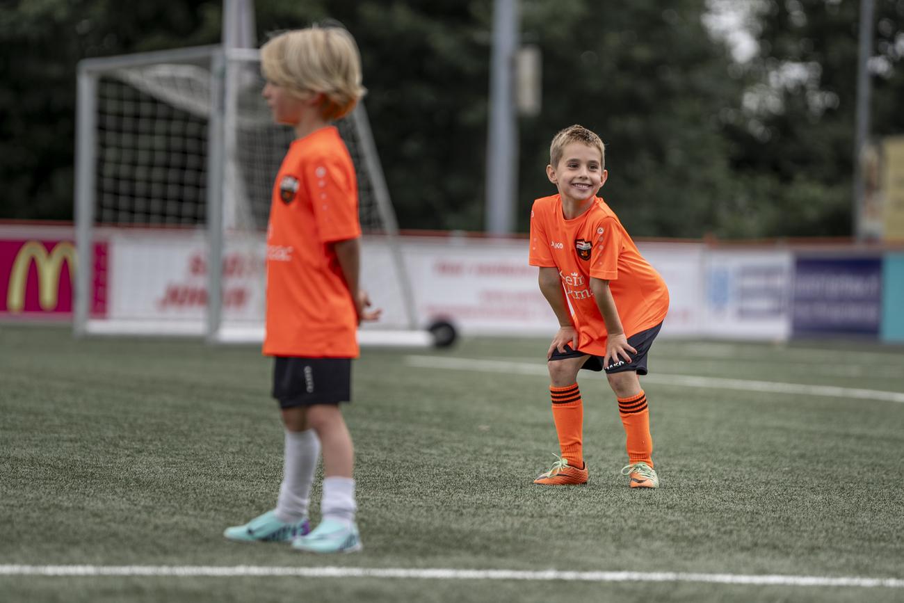 Twee jonge spelers in oranje shirts op het kunstgras, één lacht breed