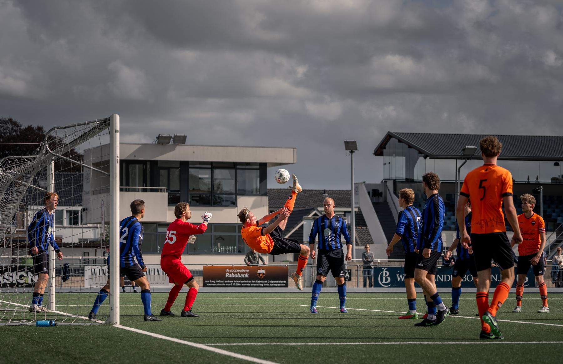 Tim de Nijs van JH 1 maakt een omhaal voor het doel, omringd door spelers in blauw-zwart