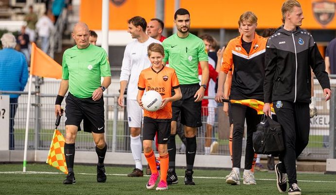 Fender loopt met de bal het veld op, tussen de scheidsrechters en de spelers